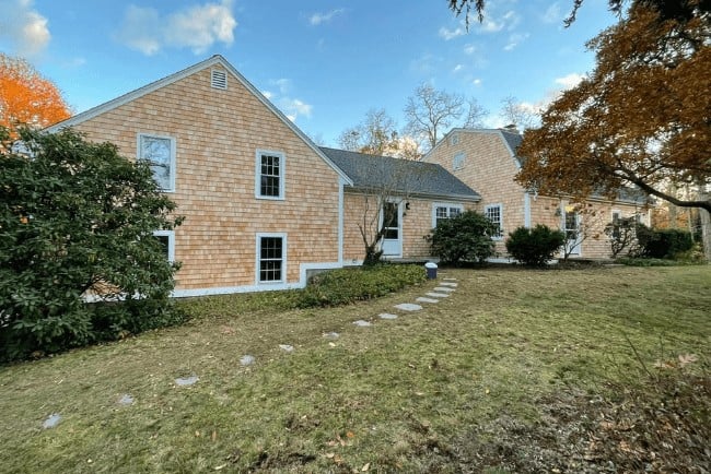 Residential home exterior in Cape Cod style, featuring shingle siding, landscaped yard, and stone pathway, highlighting Coast Carpentry's focus on home improvements and deck building services.