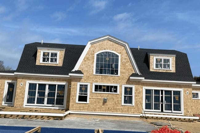 Newly constructed residential building featuring shingle siding, large windows, and a prominent gable roof, situated in a construction site setting.