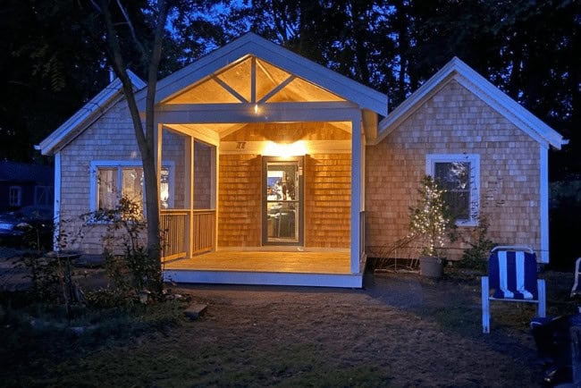 Cozy illuminated home exterior with a welcoming porch and wooden shingles, showcasing Coast Carpentry's expertise in residential construction and deck building.