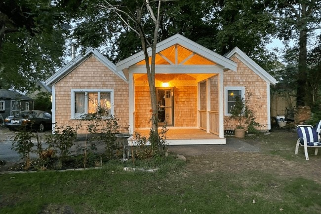 Cozy residential home with a wooden facade, illuminated porch, and landscaped front yard, showcasing construction quality and design by Coast Carpentry in Cape Cod, MA.
