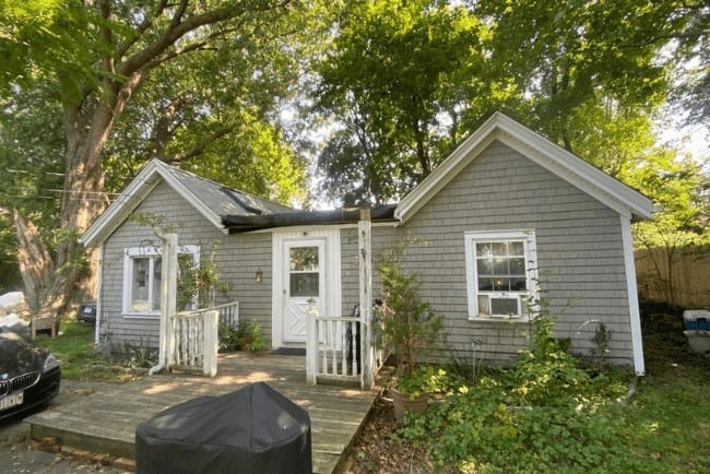 Residential home with gray siding and white trim, featuring a front porch and surrounded by greenery, highlighting Coast Carpentry's expertise in home improvements and deck building.