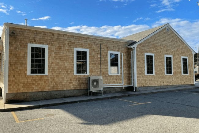 Exterior view of a newly renovated building with wooden shingle siding, multiple windows, and an air conditioning unit, reflecting Coast Carpentry's expertise in home improvement services.