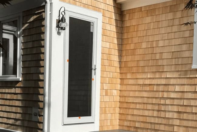Newly installed screen door with white frame on a wooden shingle exterior, showcasing Coast Carpentry's home improvement and deck building expertise.