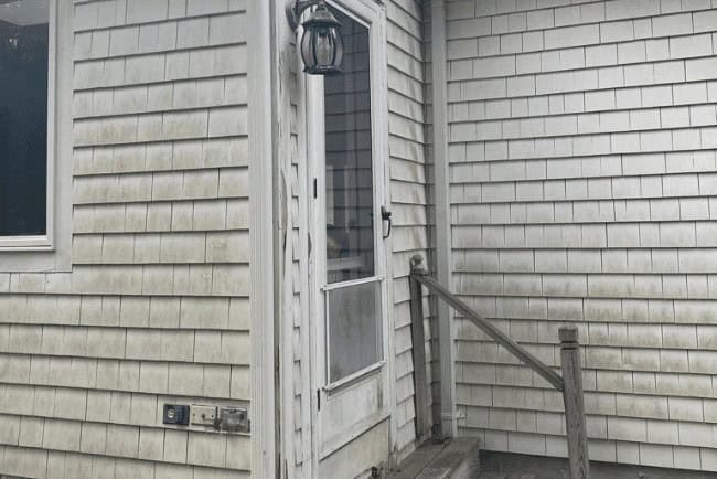 Residential entryway with a screened door, wooden steps, and a lantern, showcasing coastal-style siding, relevant to Coast Carpentry's home improvement services in Cape Cod, MA.