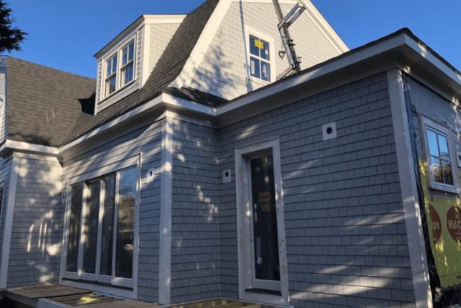 Residential construction project featuring a gray shingle exterior, large windows, and a roof with a dormer, emphasizing Coast Carpentry's home improvement services in Cape Cod, MA.