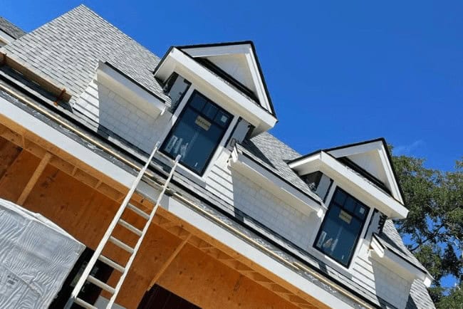 Newly constructed home with shingle roofing and large windows, showcasing carpentry details and a ladder leaning against the side, emphasizing Coast Carpentry's expertise in residential construction and home improvements.