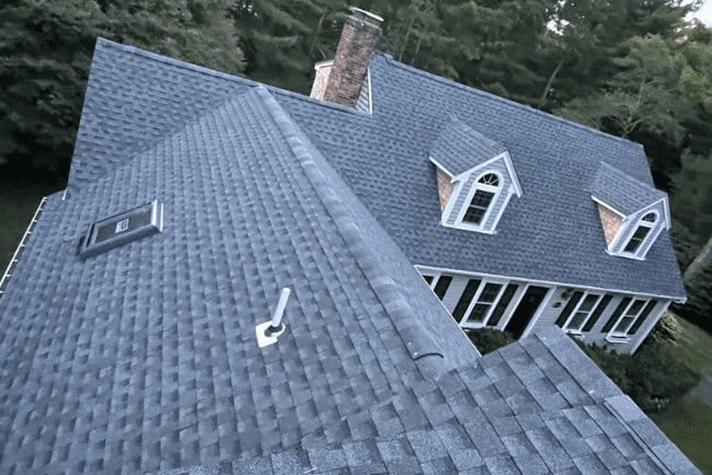Aerial view of a well-maintained residential roof with shingles, showcasing a chimney and dormer windows, relevant to Coast Carpentry's home improvement and roofing services in Cape Cod, MA.