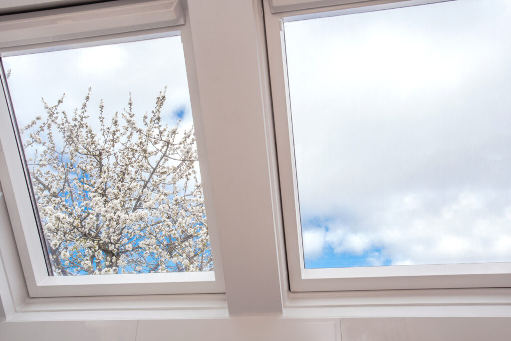 Skylights Installation services in Cape Cod- A modern open skylight,mansard window against blue sky with beautiful tree with white flowers, modern new house design, architectural detail