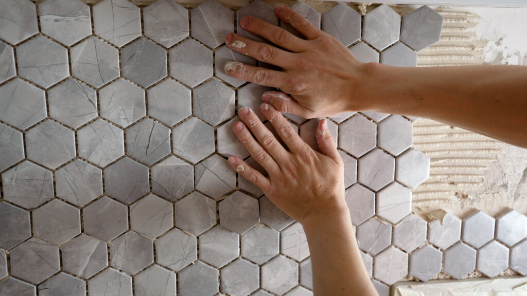 Kitchen Remodeling Services - The worker presses the tile with his hands while gluing the tile The working tiler mounts the tile on the wall, presses it with his hands The master glues a mosaic of ceramic tiles