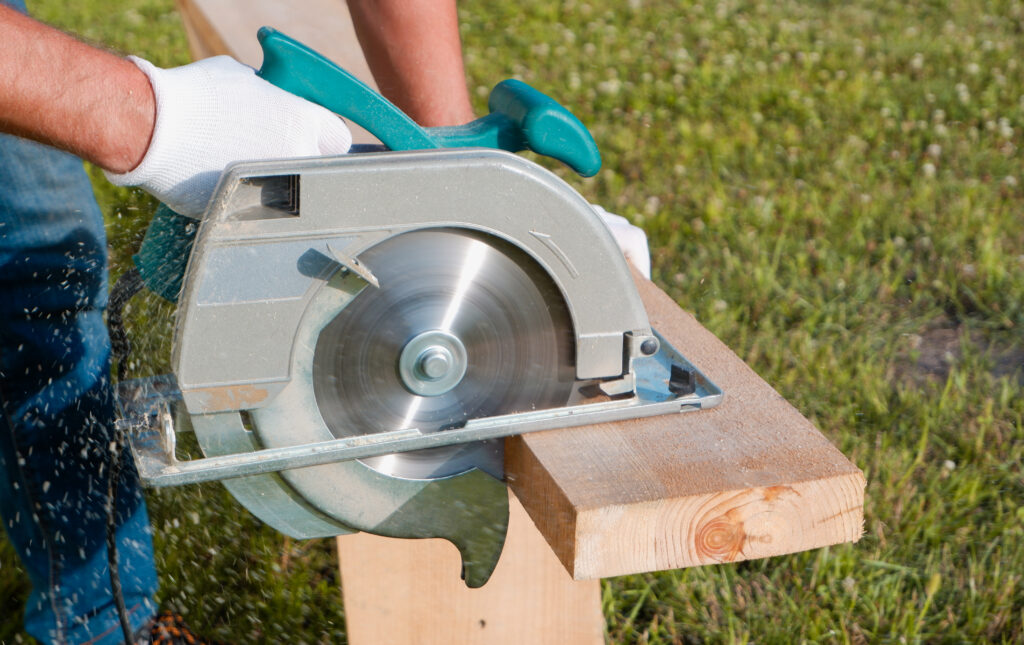 A male joiner works with a hand held circular saw A builder is sawing a board at the construction site of a new house