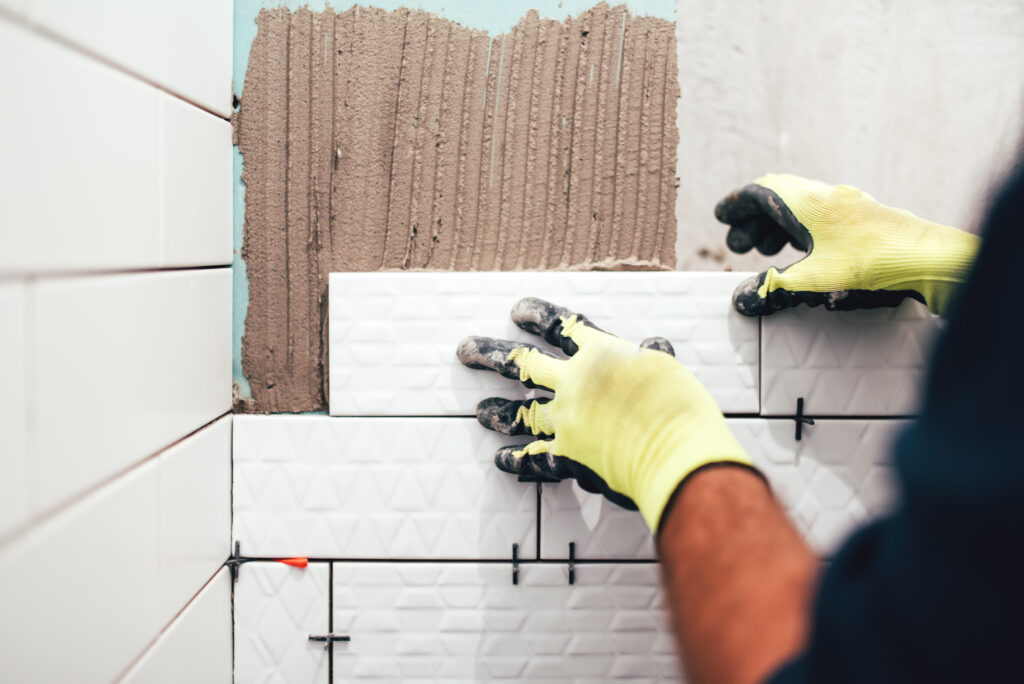 Bathrooms Remodeling - construction worker installing small ceramic tiles on bathroom walls and applying mortar with trowel