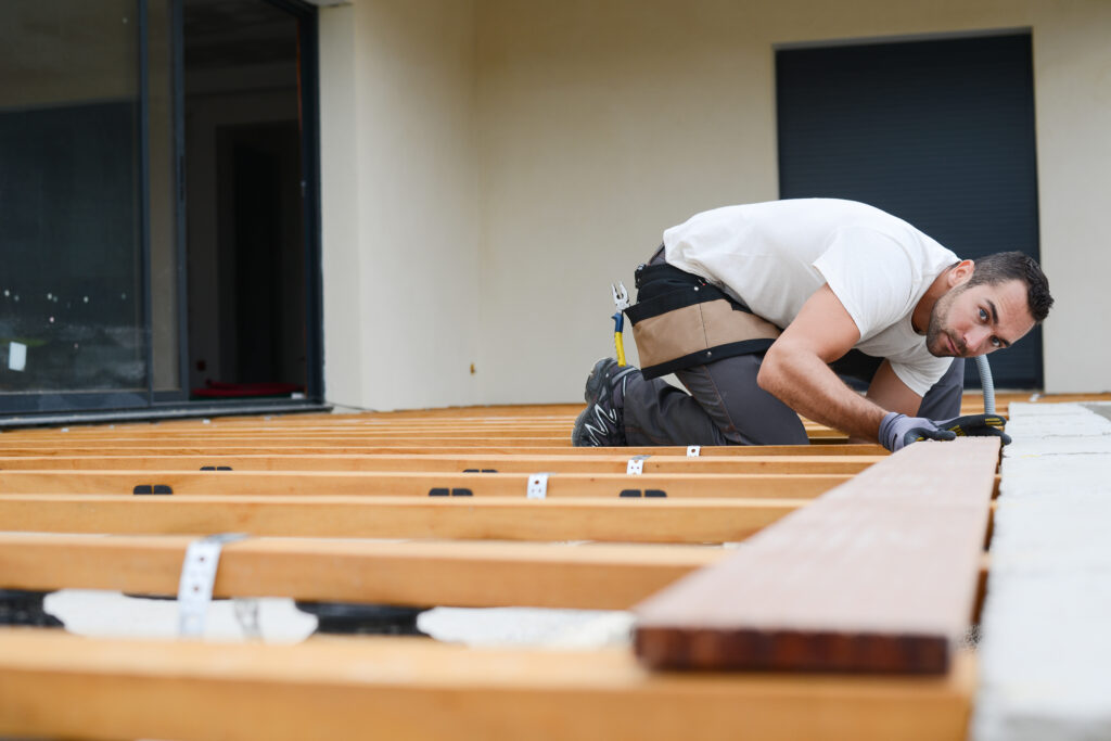 handsome young man carpenter installing a wood floor outdoor terrace in new house construction site - Cape Cod Construction Permits