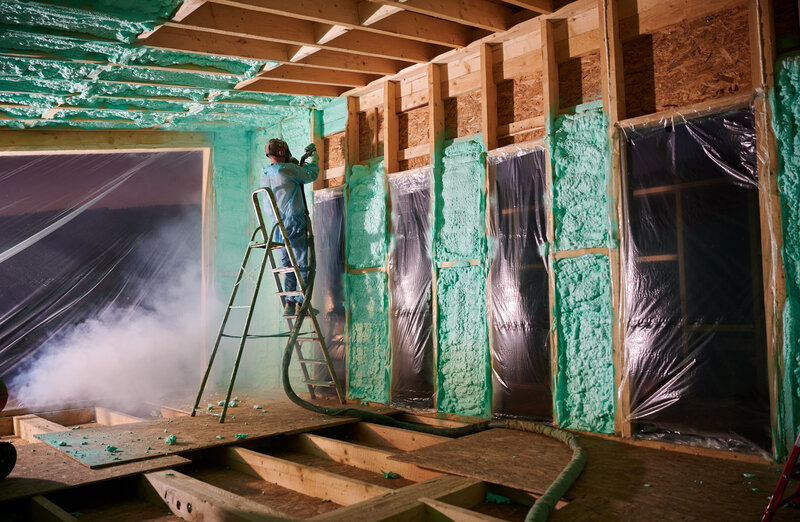 Worker spraying polyurethane foam for insulating wooden frame house