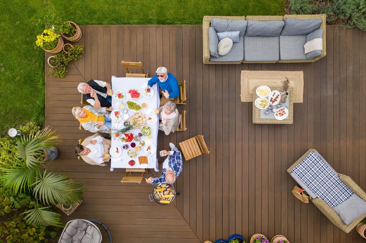 Group of people enjoying a meal on a wooden deck, surrounded by plants and outdoor seating, illustrating social gatherings in Cape Cod homes.