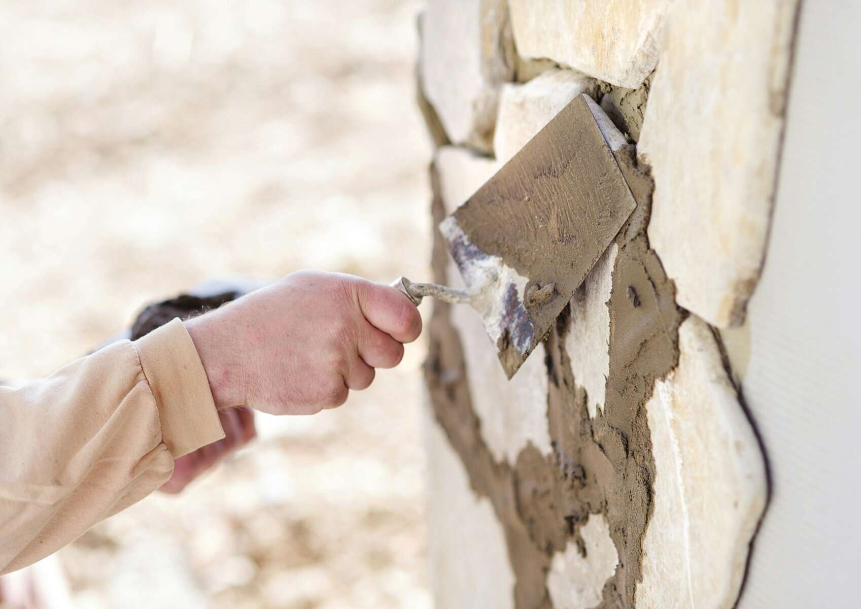 Hand applying mortar to stone masonry wall, emphasizing masonry repair and maintenance techniques relevant to construction and home improvement.