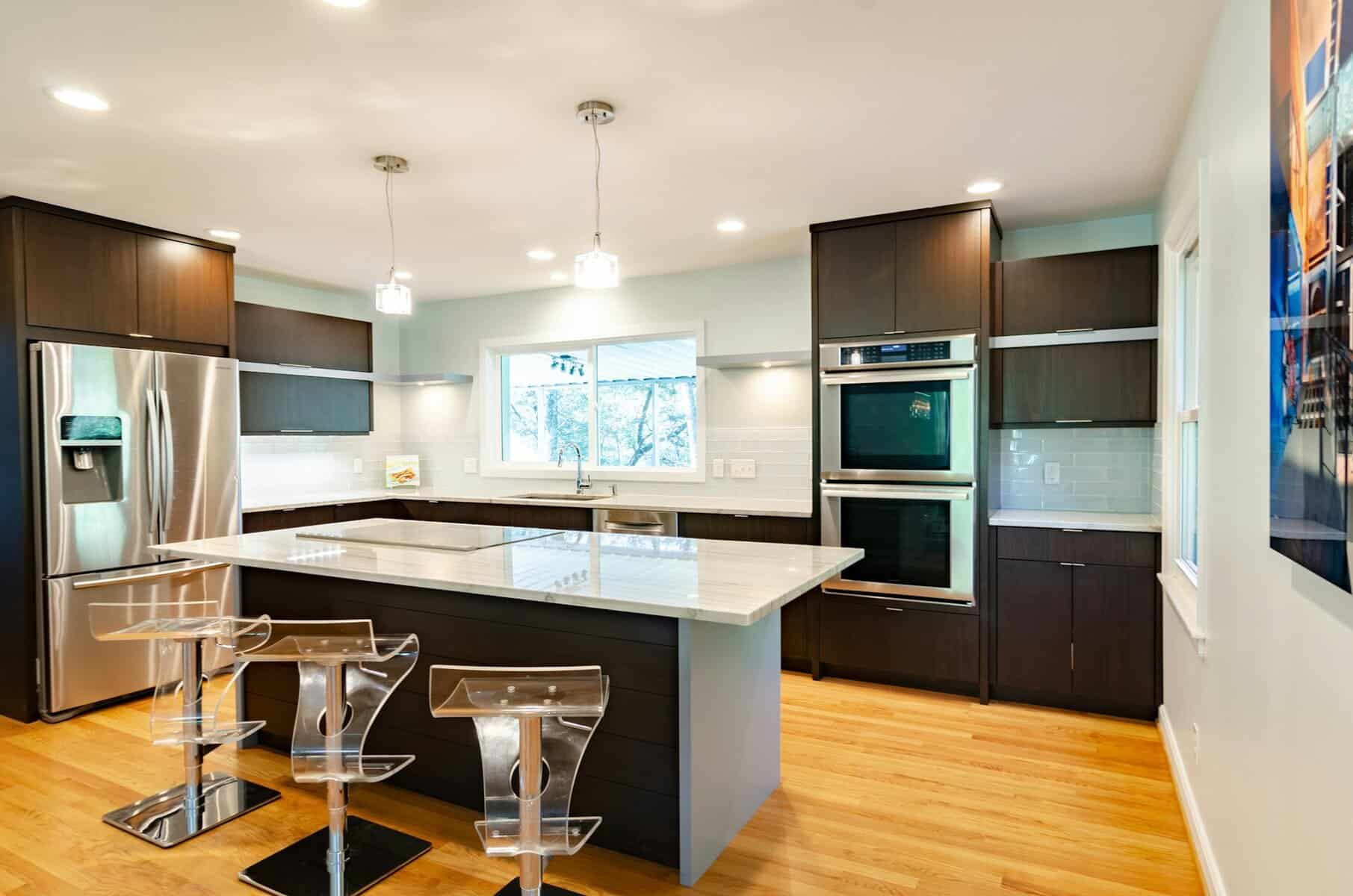 Modern kitchen design featuring dark cabinetry, stainless steel appliances, and a large island with a marble countertop, complemented by clear acrylic stools.