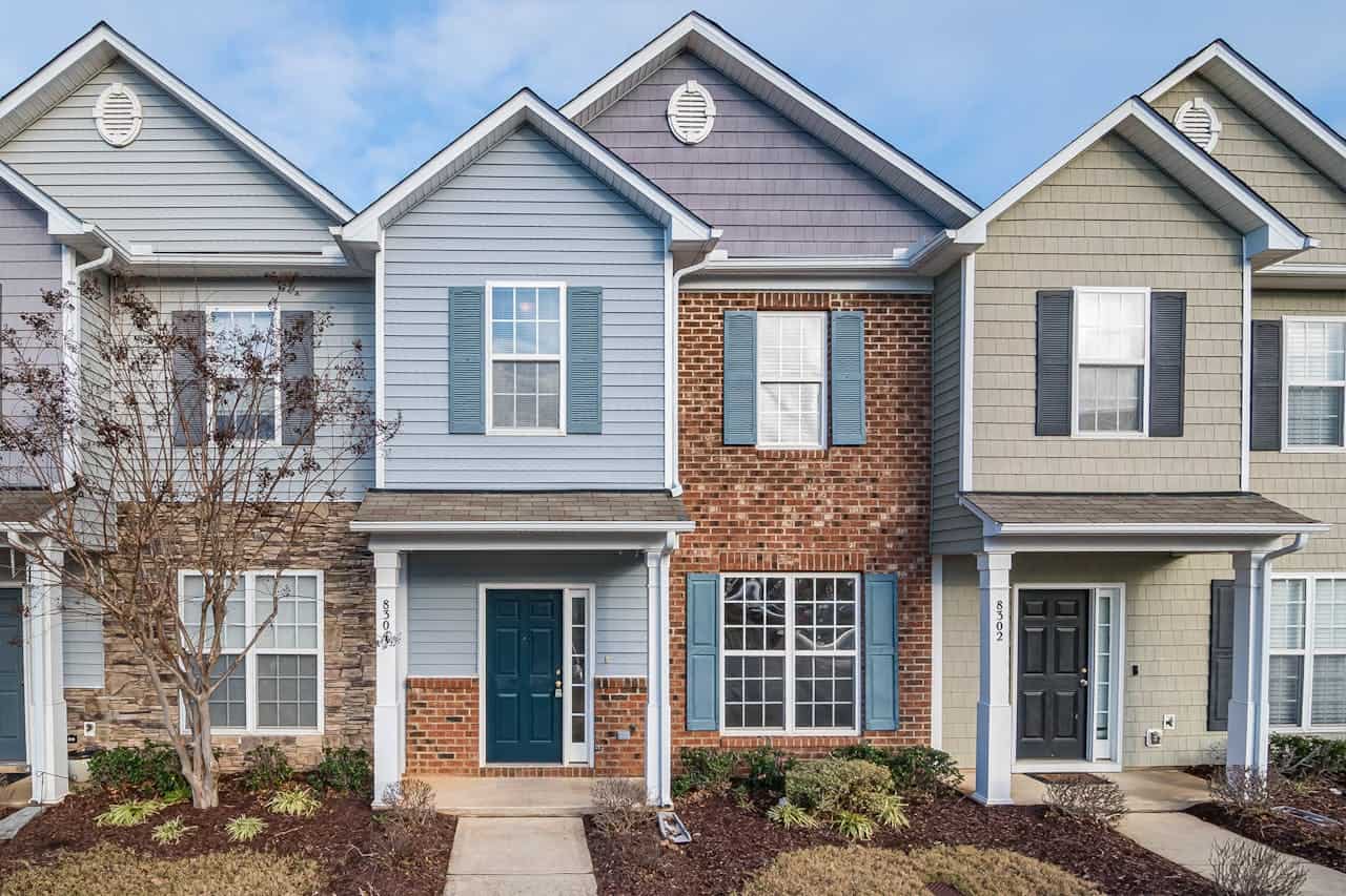 Modern townhouse exterior featuring a mix of blue siding and brick, surrounded by landscaping, illustrating residential construction and design trends.