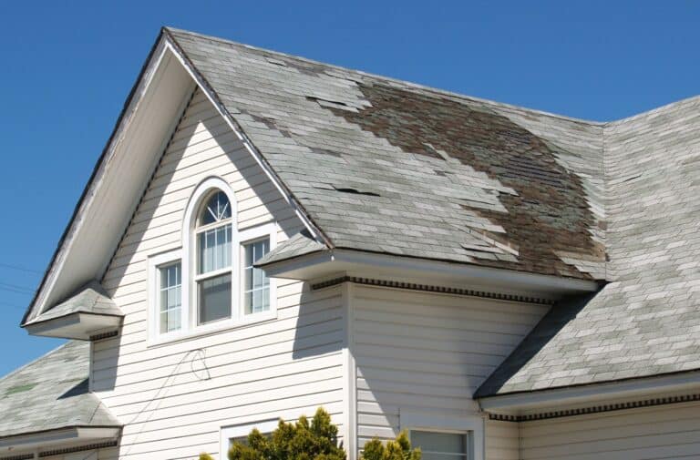Roof with damaged shingles showing curling and missing sections, indicative of storm impact and weather-related wear in Cape Cod.
