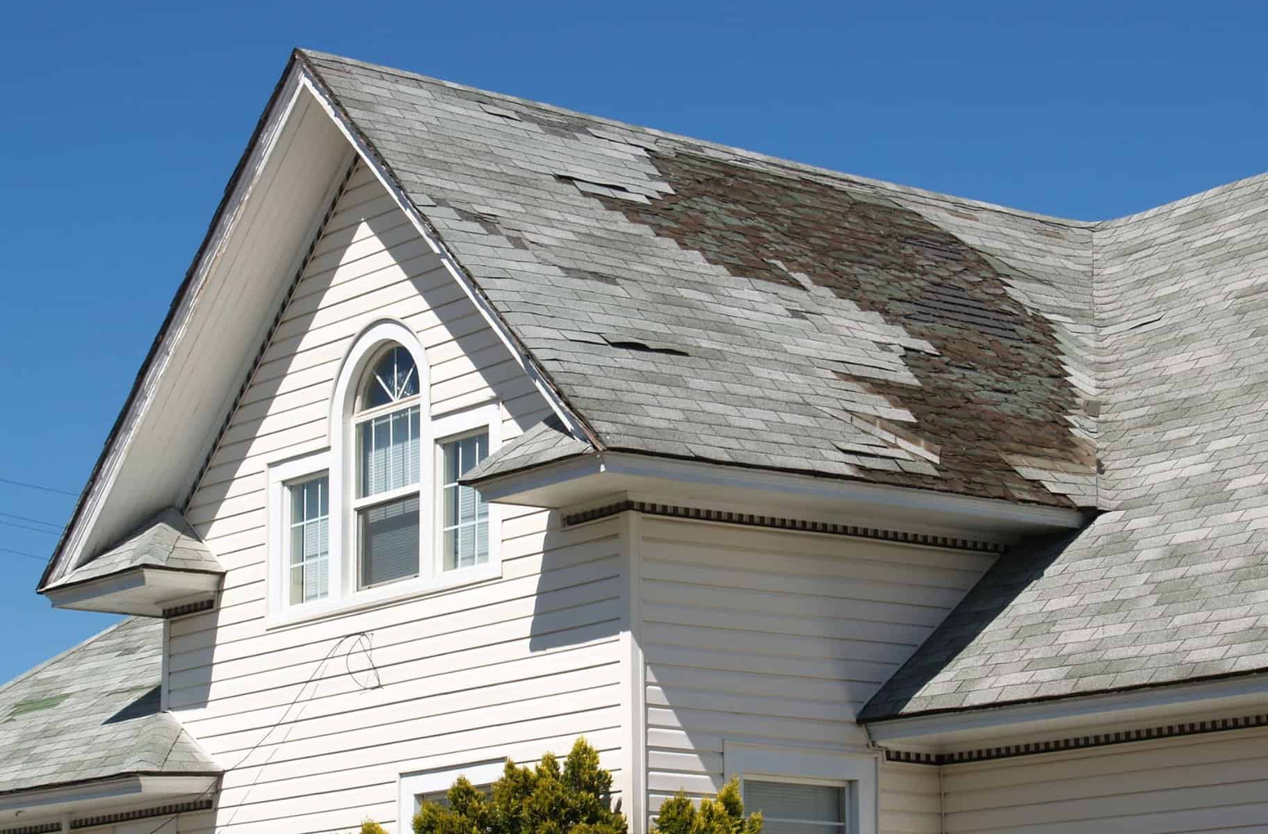 Roof with damaged shingles and discoloration, illustrating storm-related roof damage in a residential setting.