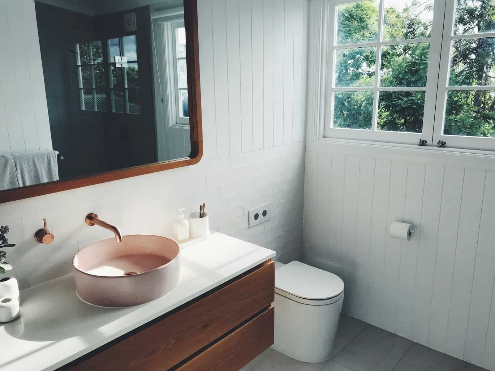 Modern bathroom interior featuring a pink circular sink, wooden cabinetry, and large window with greenery outside, highlighting stylish design elements for home improvement.