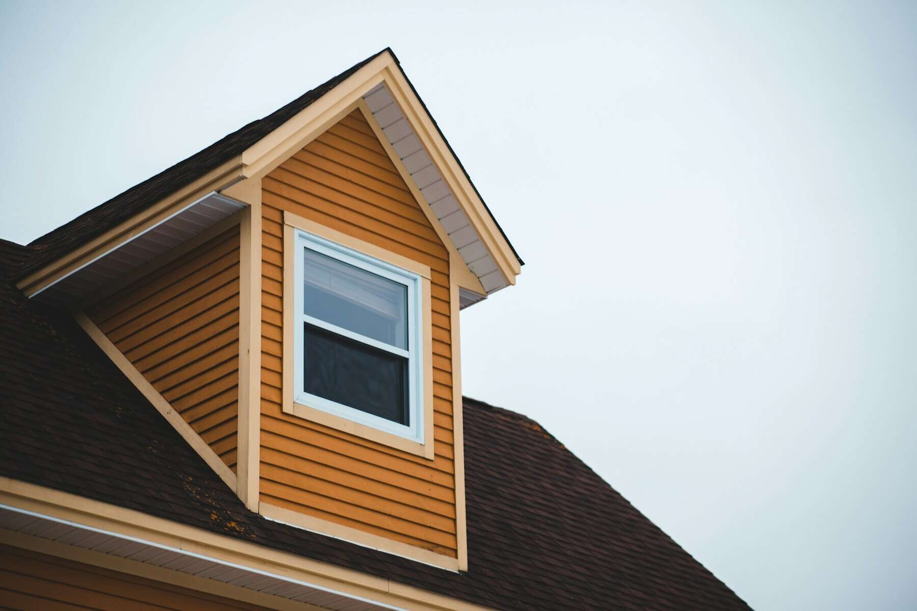 Roof corner of a Cape Cod-style home featuring orange siding and a white window, illustrating residential construction and home improvement themes.