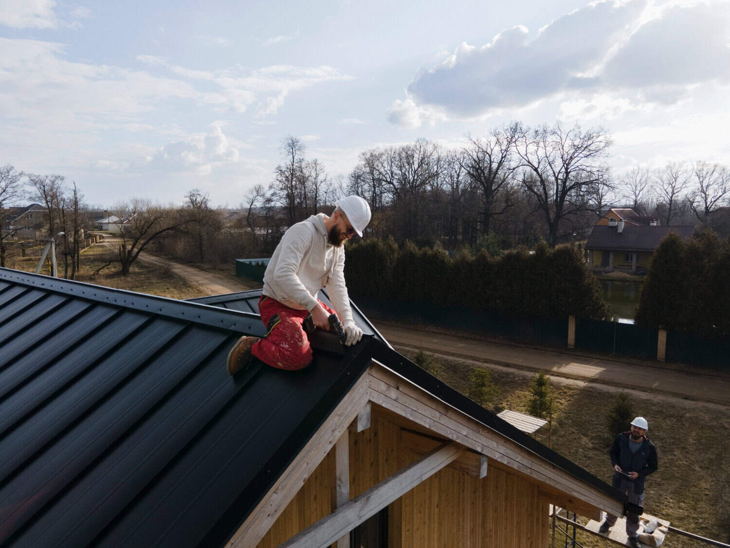 Roof repair in progress with a worker installing metal roofing on a residential home, showcasing construction techniques and maintenance for exterior home improvement.