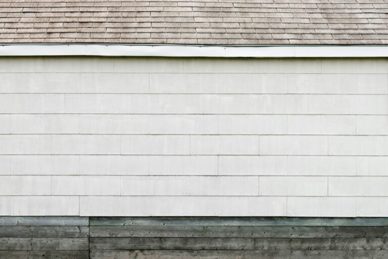 Roof with gray shingles above a white wall, representing roofing materials relevant to Cape Cod homeowners facing shingle damage.