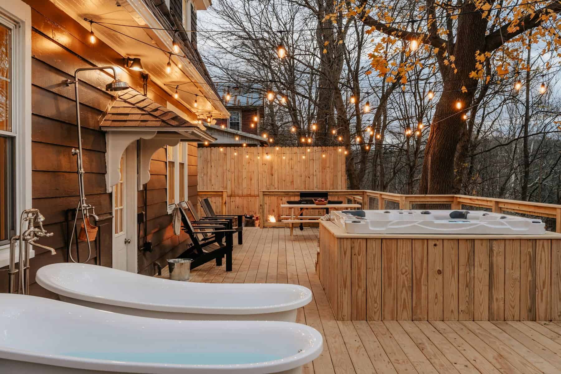 Outdoor deck with two white bathtubs, hot tub, wooden seating, and string lights illuminating a cozy atmosphere, showcasing home improvement ideas for residential spaces.