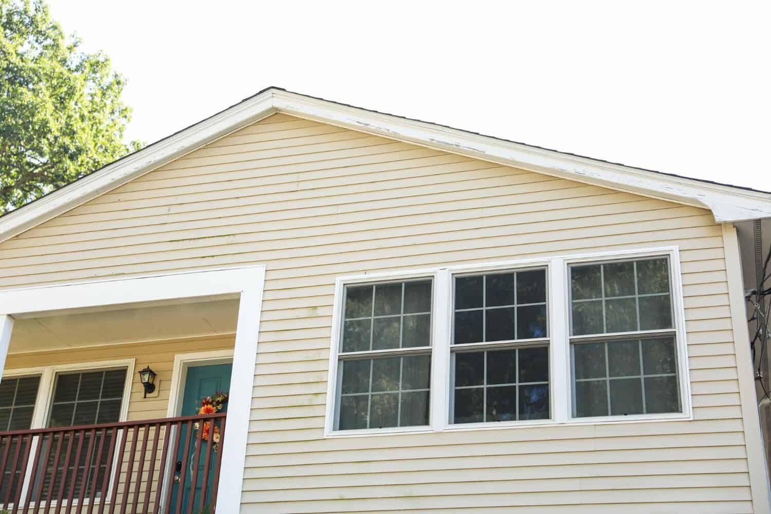 Home exterior featuring beige siding, two large windows, and a blue front door with a decorative wreath, illustrating potential siding maintenance and repair topics.