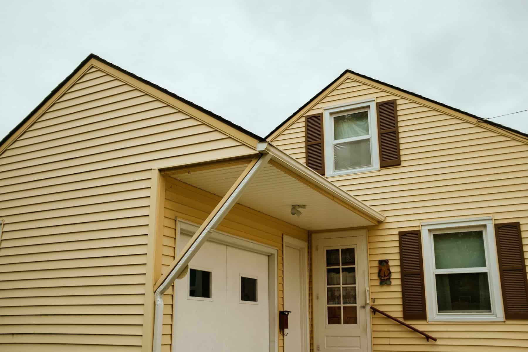 Residential home exterior featuring yellow siding, brown shutters, and a covered entrance, relevant to construction and home improvement topics.