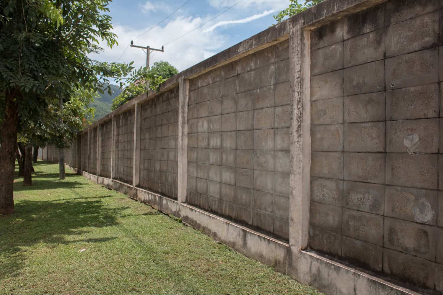 Leaning concrete retaining wall in a residential landscape with grass and trees, illustrating structural issues relevant to construction and home improvement.