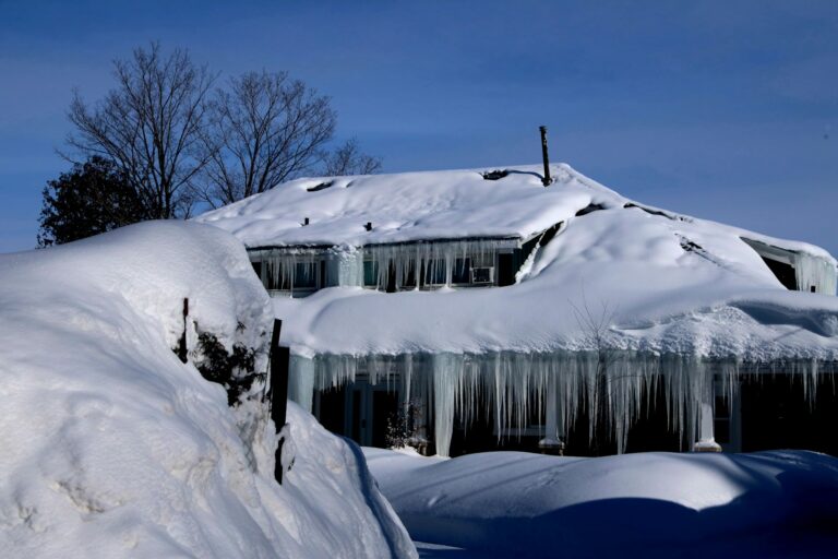 House covered in snow with large icicles hanging from the roof, highlighting winter weather challenges for homeowners in Cape Cod.