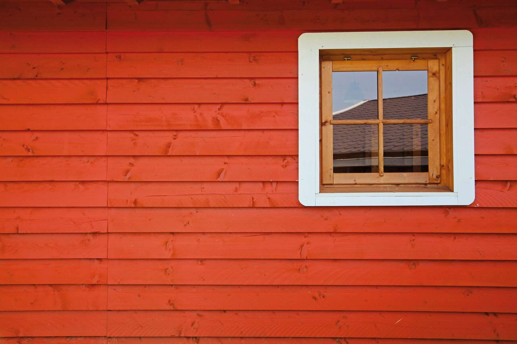 Red wooden siding with a wooden window framed in white, highlighting construction and home improvement themes relevant to Cape Cod homes.