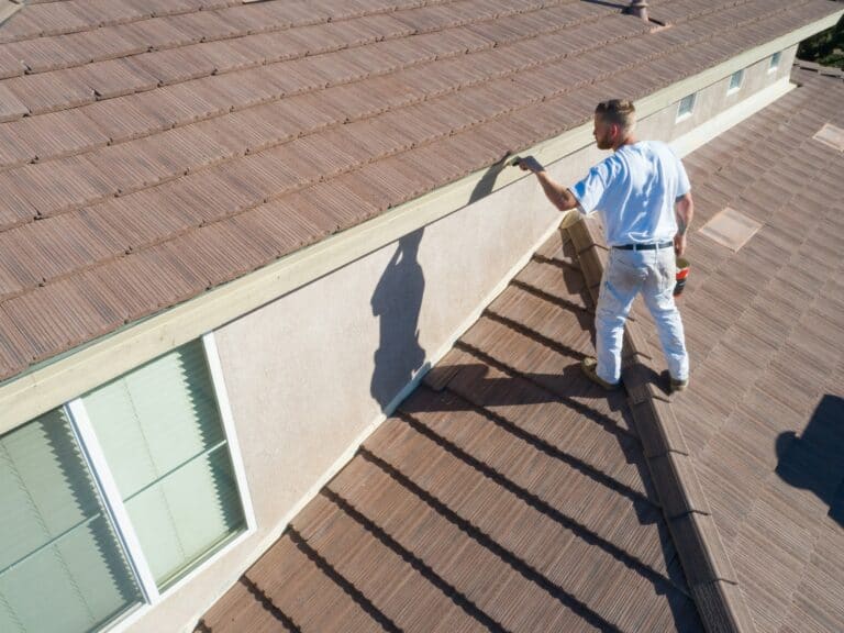 Man performing roof maintenance on a residential building, focusing on roof shingles and gutter, emphasizing home upkeep in Cape Cod’s seasonal weather.