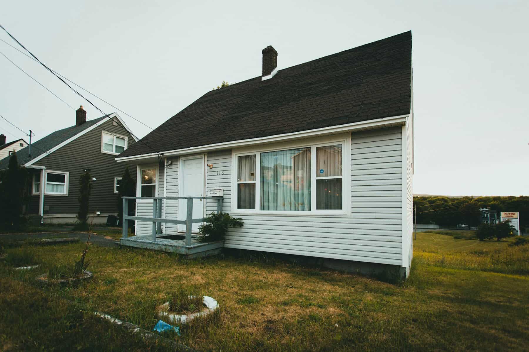 Single-story residential home with gray siding and a front porch, surrounded by grass and neighboring houses, relevant to construction and home improvement topics.