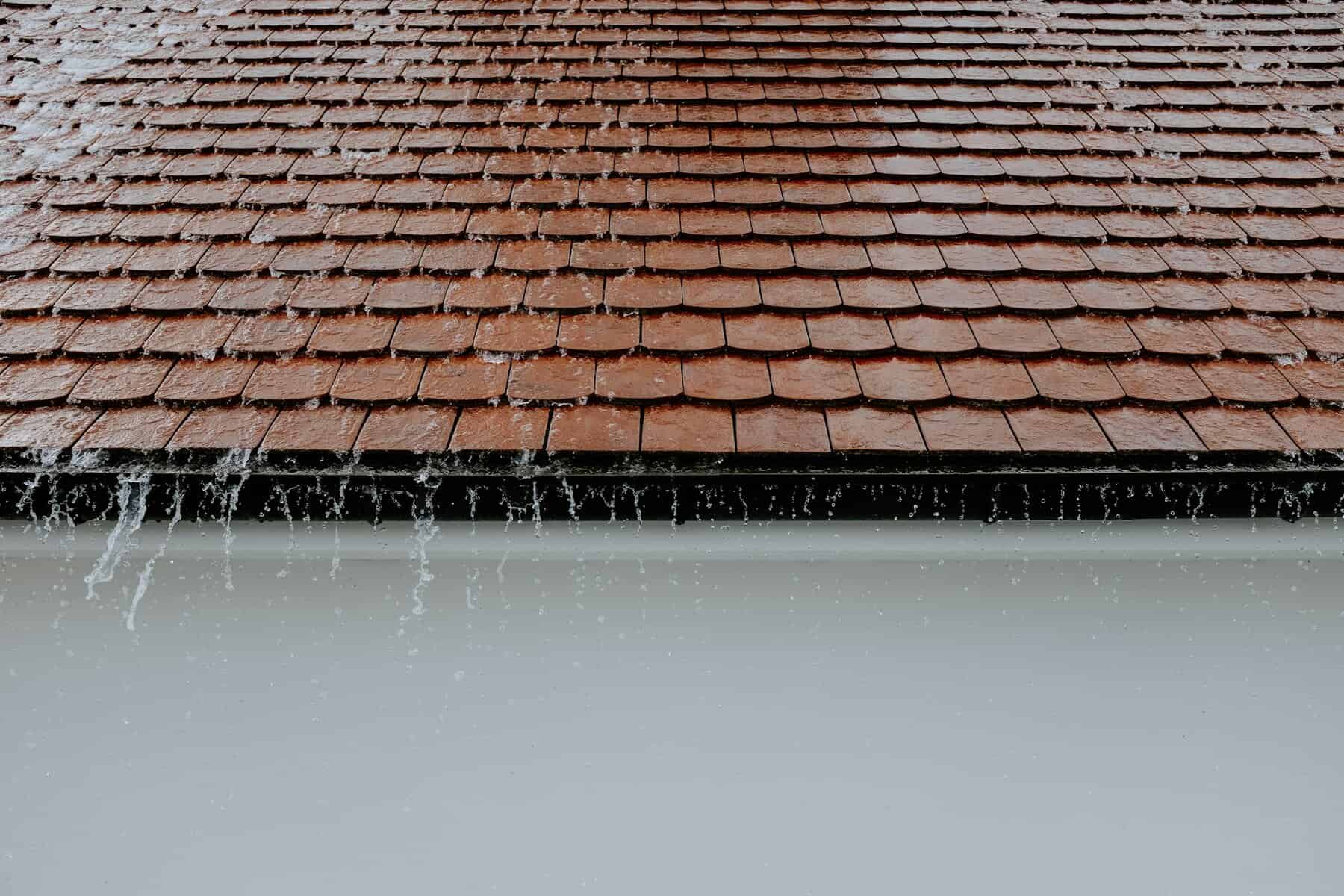 Roof with brown shingles and water cascading off the edge, illustrating roofing conditions relevant to Cape Cod's weather challenges.