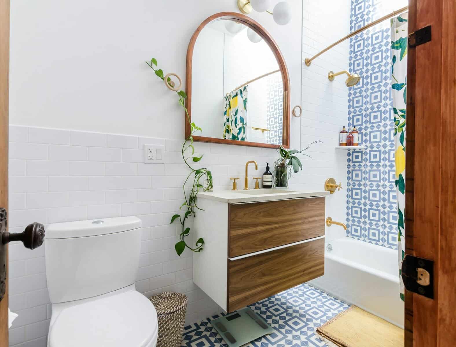Modern bathroom interior with white tiles, wooden vanity, gold fixtures, and patterned blue shower curtain, highlighting Cape Cod remodeling aesthetics.