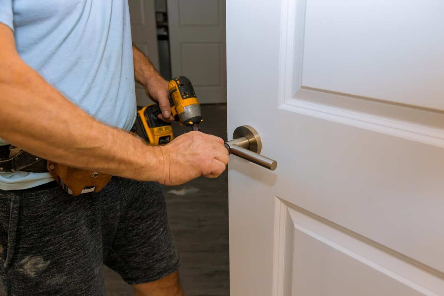 Man using a power drill to install a door handle on a white interior door, illustrating door installation for improved energy efficiency in Cape Cod homes.