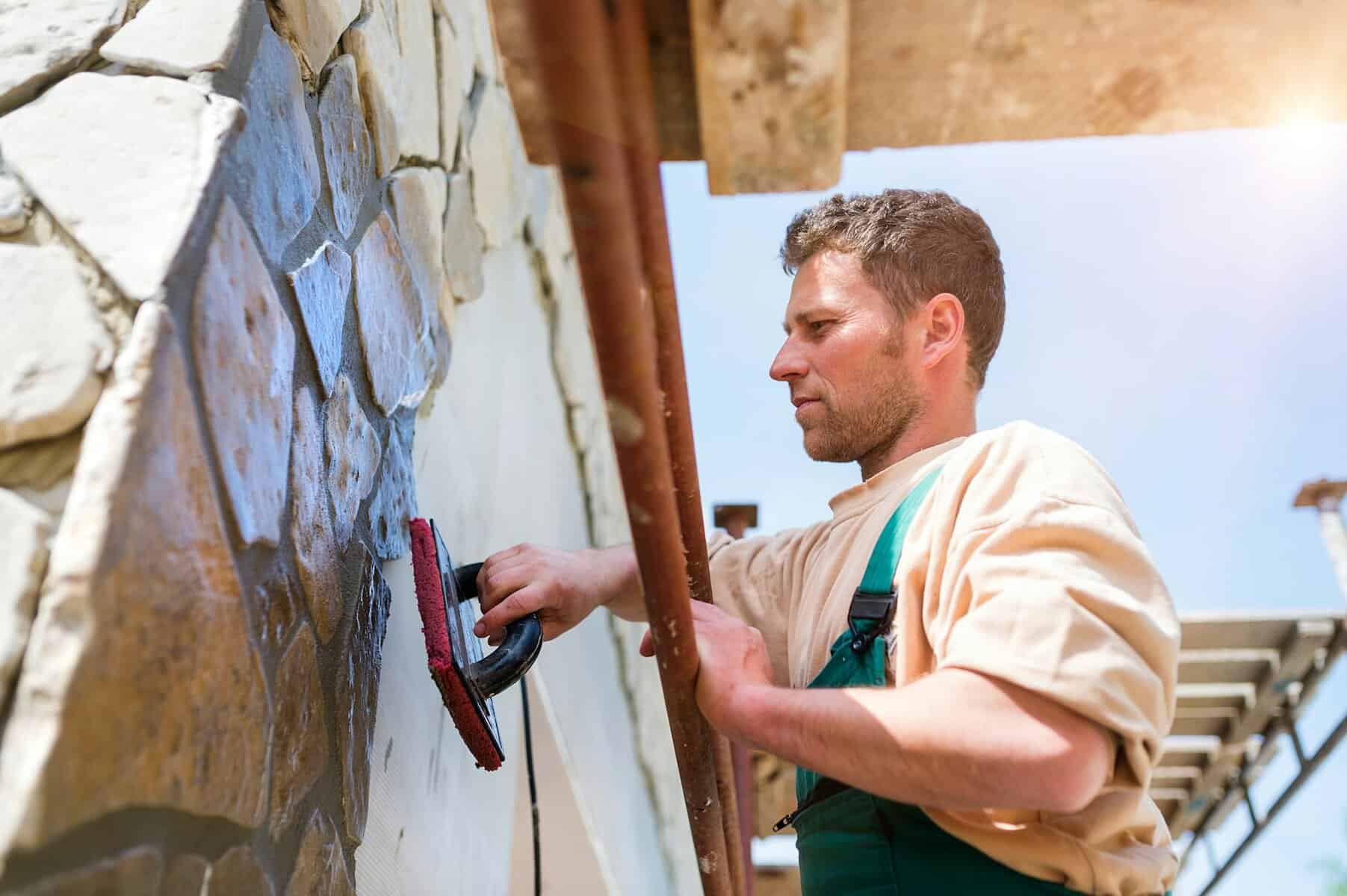 Masonry worker applying finishing touches to stone wall, illustrating local craftsmanship relevant to Cape Cod construction and remodeling services.