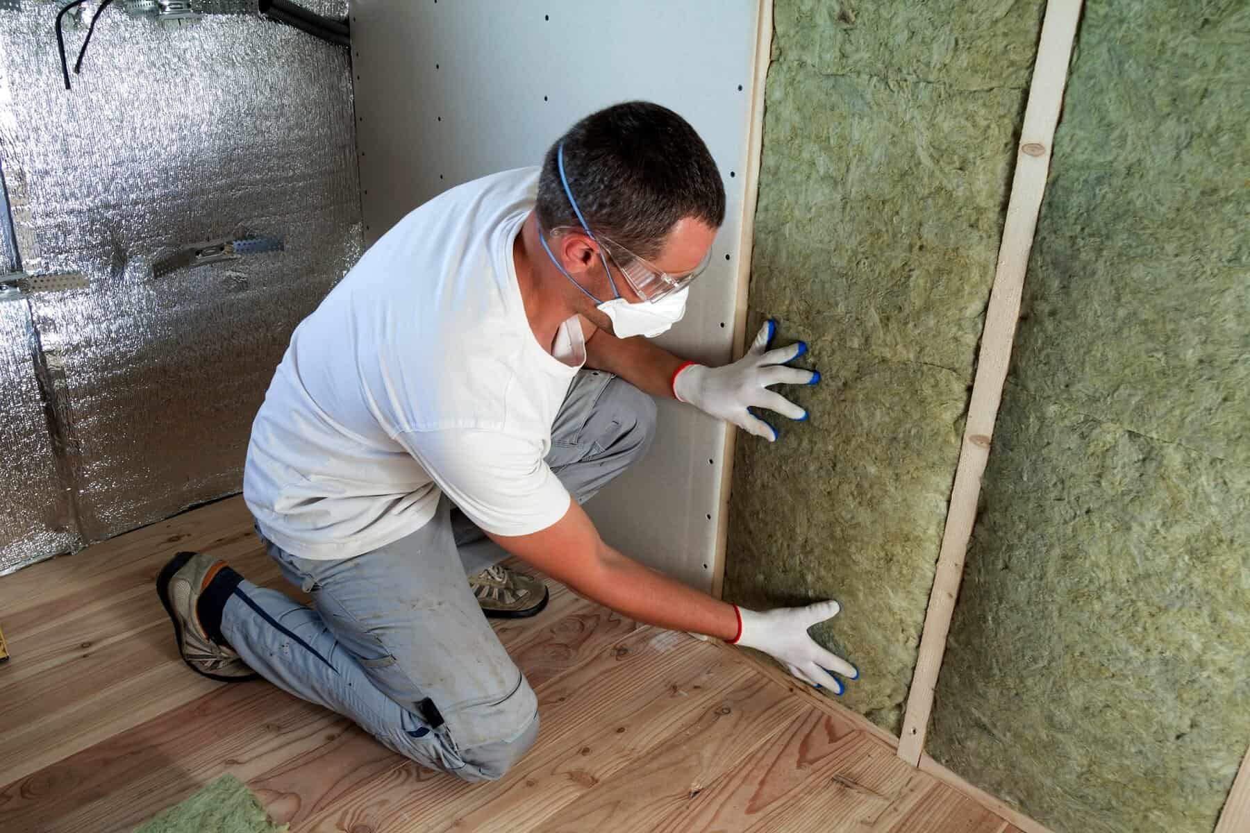 Man installing insulation in a residential construction setting, emphasizing the importance of insulation for Cape Cod homes before cold weather.