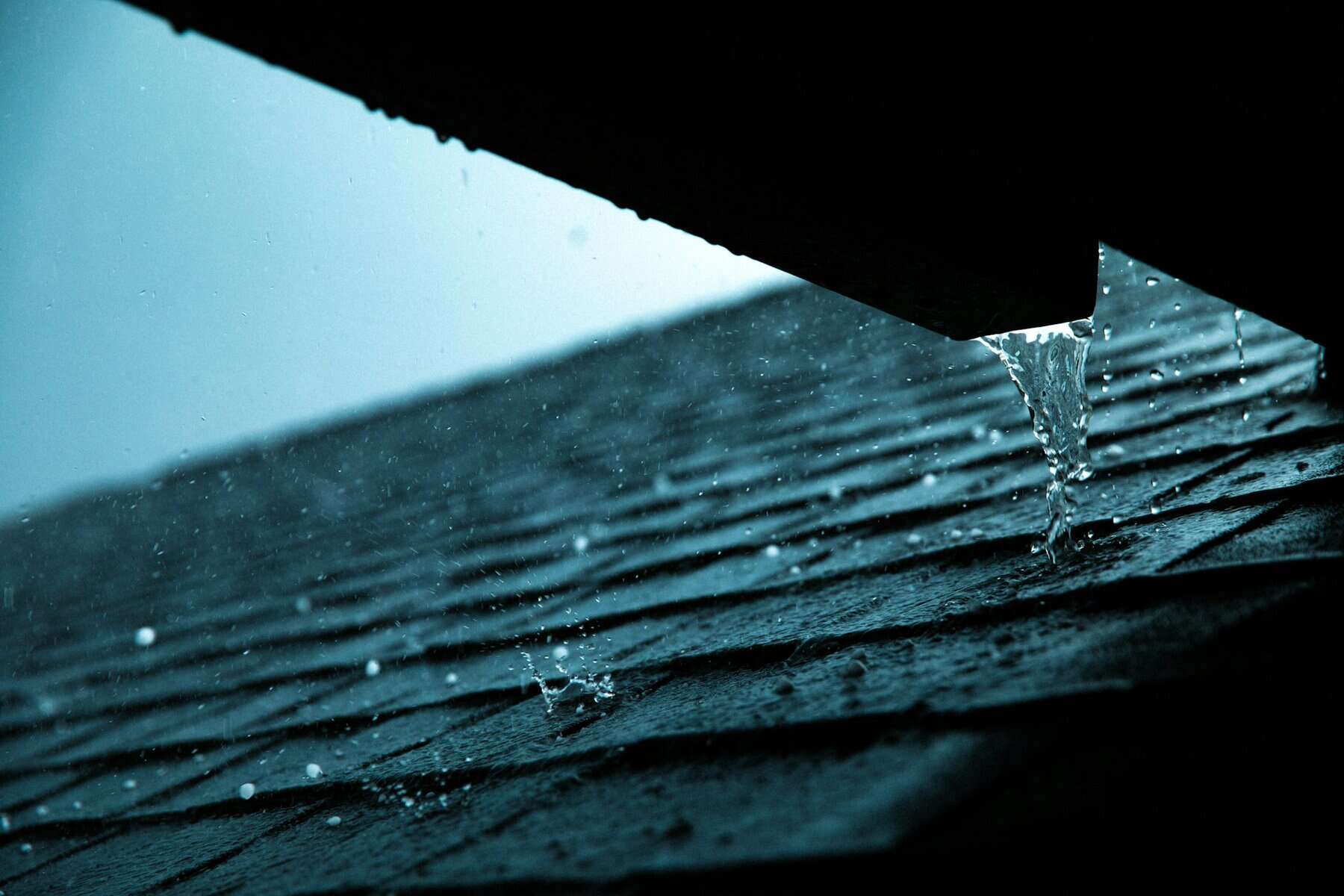 Rainwater cascading from a roof onto shingles, illustrating the impact of fall rain on Cape Cod roofing jobs.