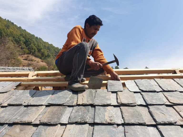 Man installing roof shingles on a house, focusing on maintenance and repair in preparation for storm season in Cape Cod.
