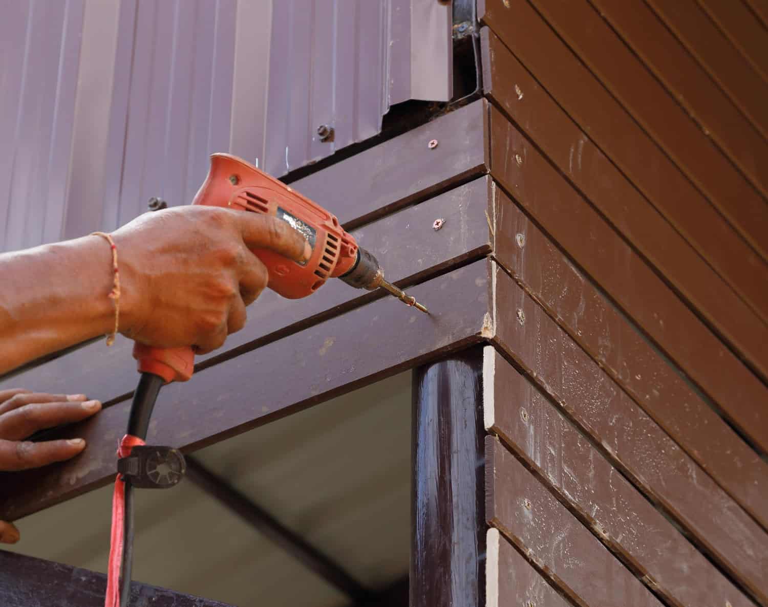 Hands using a power drill to install siding on a Cape Cod home, highlighting construction techniques relevant to siding installation.