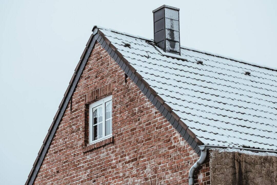 Older brick home with a snow-covered roof and chimney, highlighting winter masonry conditions relevant to Cape Cod home maintenance.