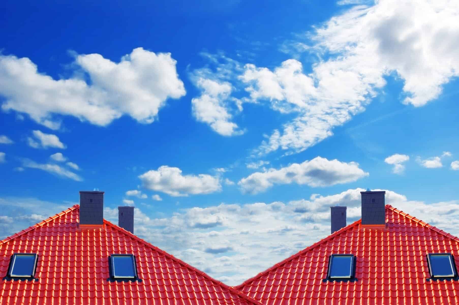 Red-tiled roofs with skylights and chimney stacks under a blue sky with clouds, relevant to Cape Cod roofing and home improvement.