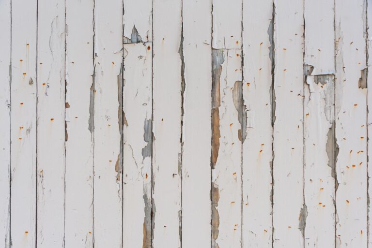 Damaged white siding with peeling paint and exposed wood, highlighting wear from harsh winter conditions on Cape Cod.