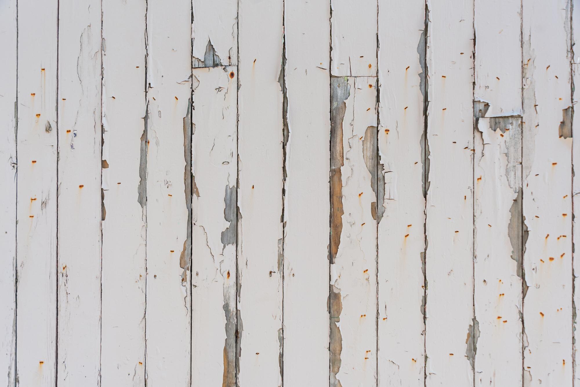 Damaged white wooden siding with peeling paint and rust spots, illustrating the need for home improvement services by Coast Carpentry Construction.