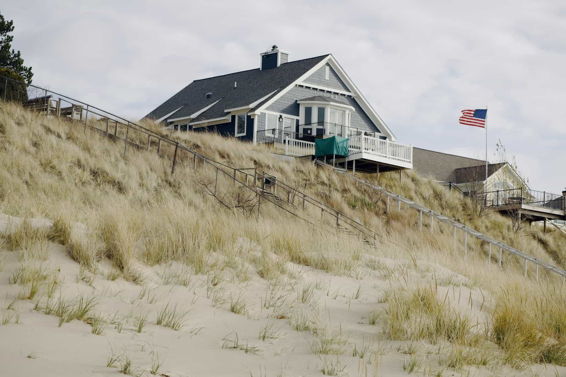 Shingled Cape Cod home with a white railed deck above beach grass, the kind of deck Coast Carpentry builds